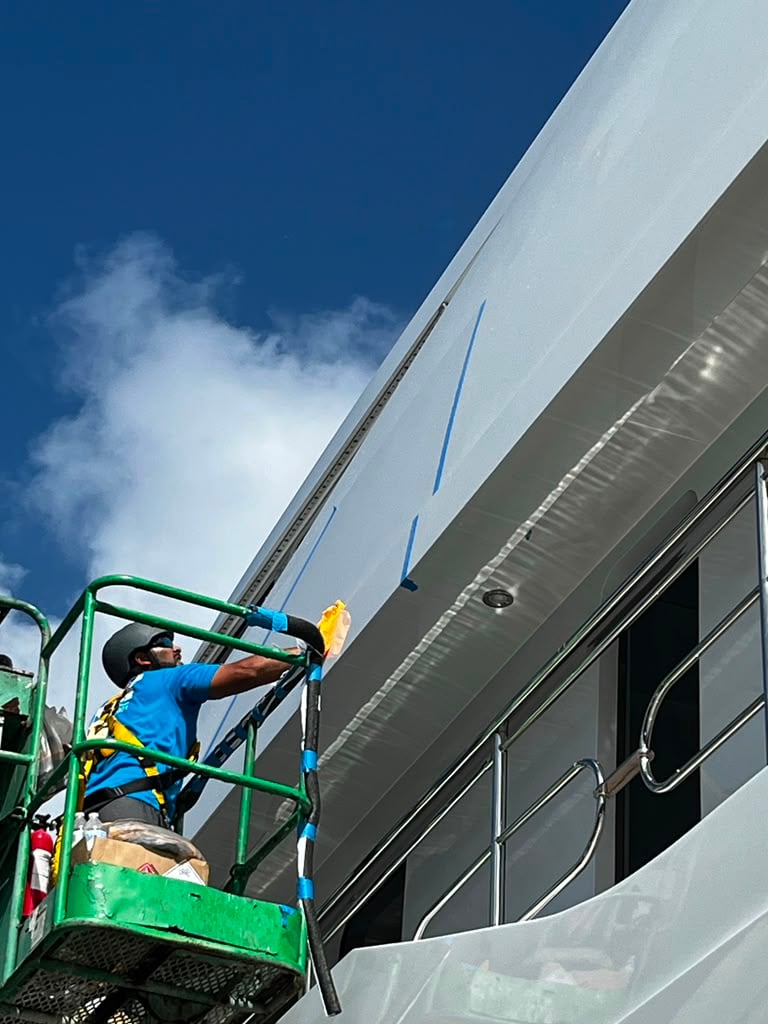 Technician detailing a yacht hull from a lift